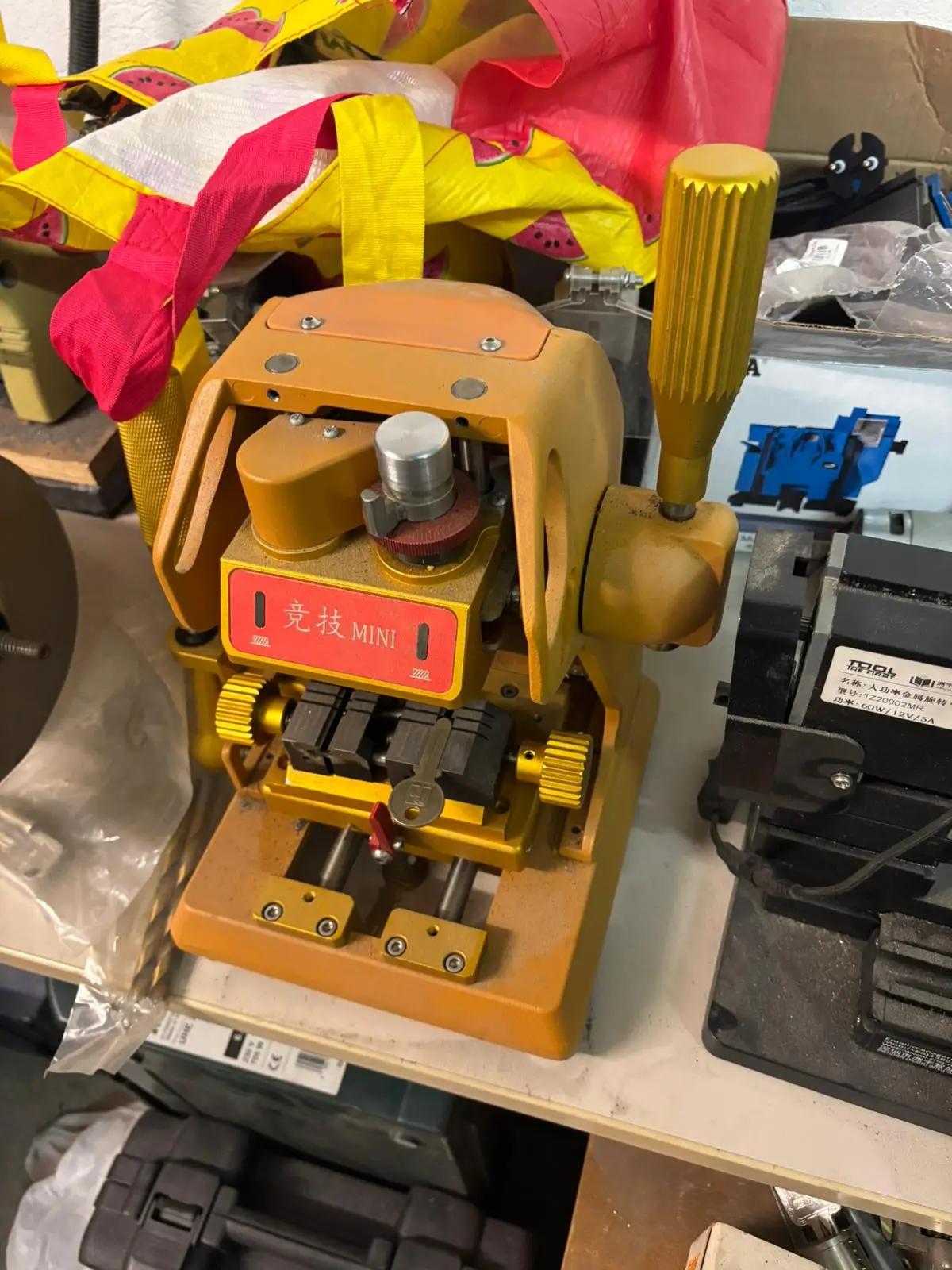 Petite machine de duplication de clés jaune avec levier latéral, installée sur un établi d’atelier.