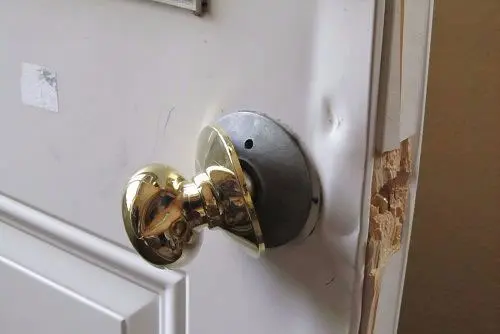 Porte endommagée après une effraction avec poignée desserrée et cadre de porte abîmé